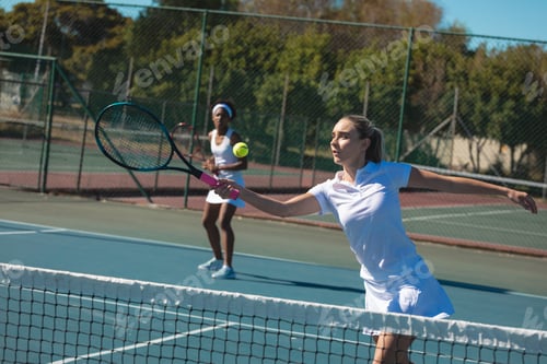 Preview: Caucasian female athlete playing tennis with african american doubles partner at court on sunny day