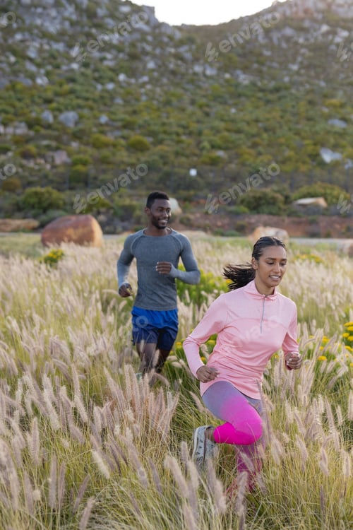 Preview: Fit african american couple in sportswear running through tall grass