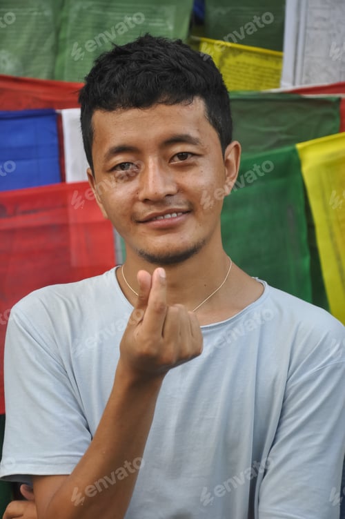 Preview: Closeup shot of a happy Tibetan guy making Korean love sign with his hand with looking at camera