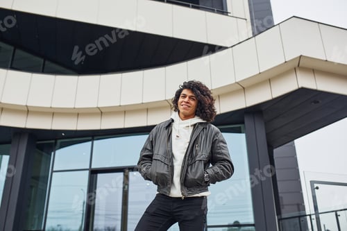 Preview: Handsome young man with curly black hair posing for the camera on the street against building