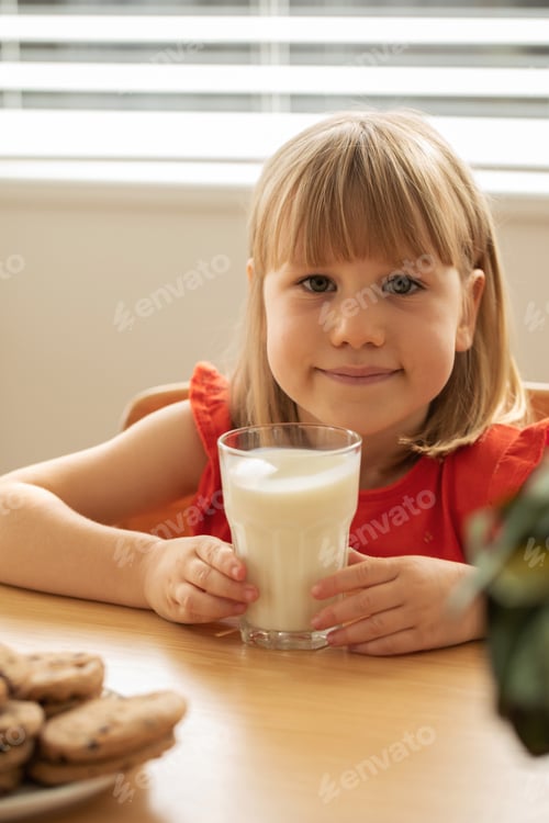 Preview: Cheerful girl enjoying fresh milk and homemade cookies, perfect for a wholesome snack time.