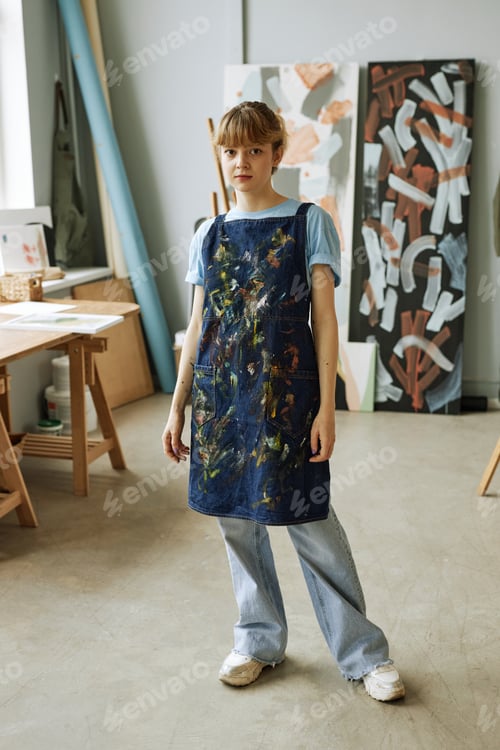 Preview: Young pretty woman in casualwear and apron standing in studio of arts