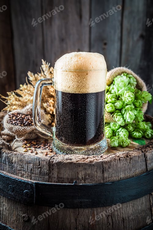 Preview: Pint of dark beer with foam on barrel. Brewing industry.