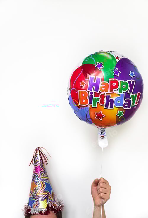 Preview: Person is wearing a birthday party hat and holding HAPPY Birthday balloon against white background