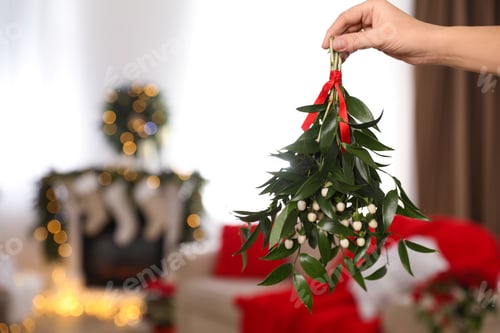 Preview: Woman holding mistletoe bunch in room with Christmas decorations, closeup. Space for text