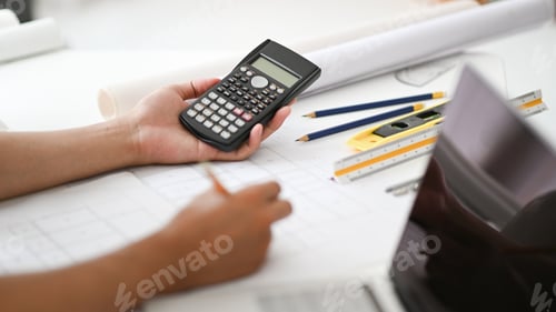 Preview: Hand holding a calculator and pencil checking house plans,engineers are calculating house scale.