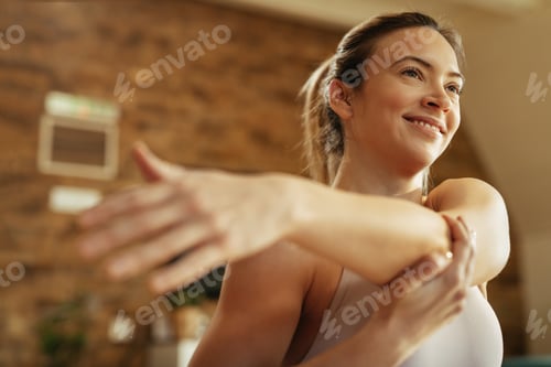 Preview: Below view of female athlete stretching her arms while exercising at home.