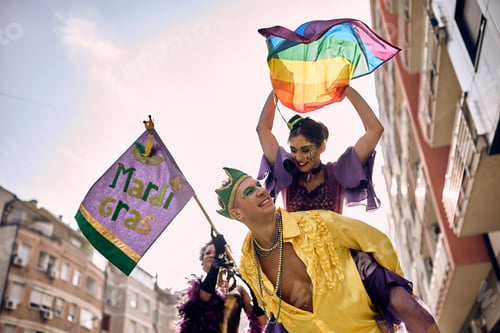 Preview: Below view of couple in piggybacking on street carnival during Mardi Gras celebration.