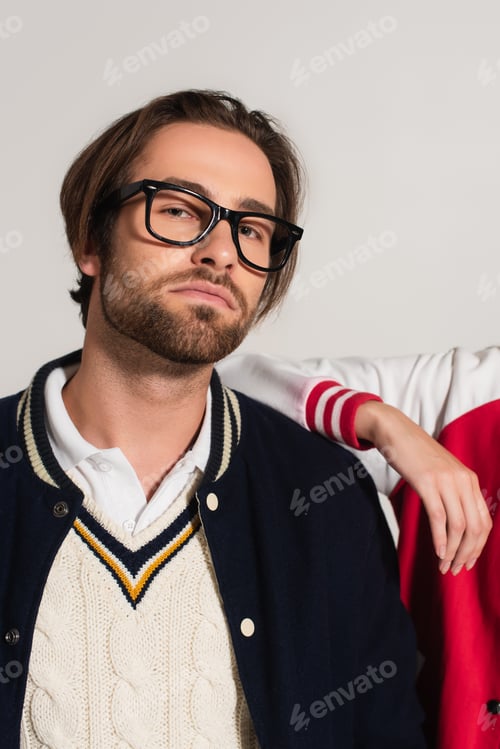 Preview: stylish man in eyeglasses looking at camera near woman leaning on his shoulder isolated on grey