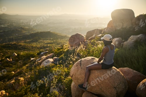 Preview: fit female hiker at top of mountain sitting on rock watching sunset with san diego in the distance