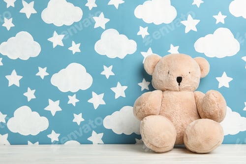 Preview: Teddy bear on white wooden table near wall with painted blue sky, space for text. Baby room interior