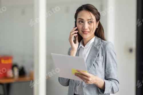 Preview: Young smiling Business asian woman talking on mobile phone, standing in workplace office wi