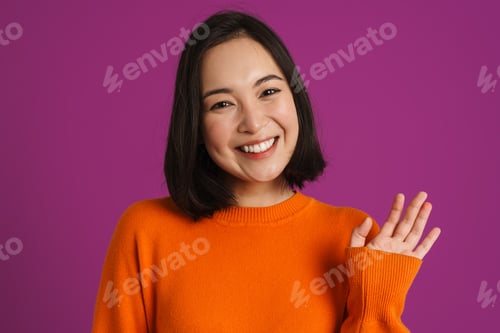 Preview: Young asian woman smiling and waving hand at camera