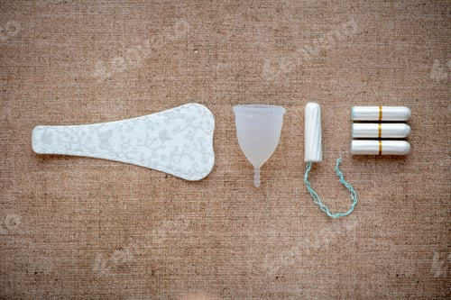 Preview: Female hygiene products lay out on a bed. Paracetamol, Sanitary pad, tampon, Chocolate,