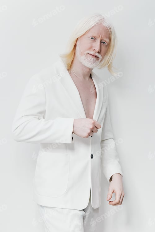Preview: Elderly man with long white hair in a stylish white suit, standing against a bright white background