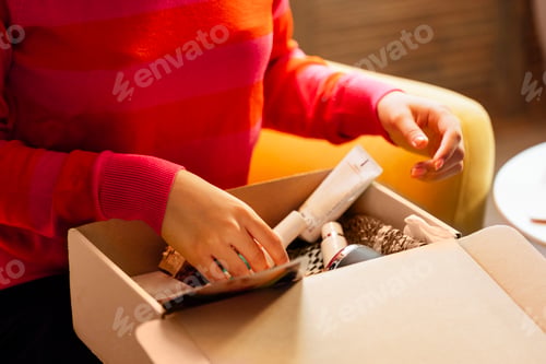 Preview: A young attractive African woman in casual clothing is unpacking a beauty box with cosmetic product