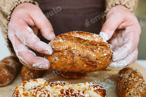 Preview: Closeup hands holding freshly baked loaf of bread in bakery