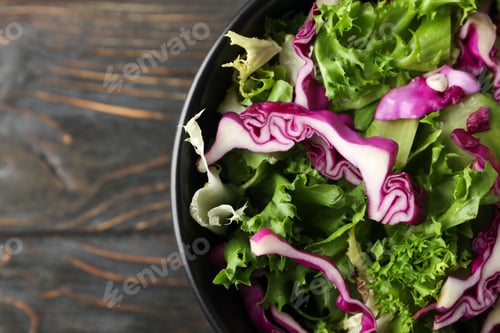 Preview: Black bowl with fresh vegetable slices on wooden background, close up