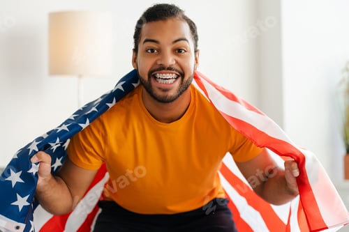 Preview: African American soccer fan with braces, shouting and celebrating a goal, holding a USA flag