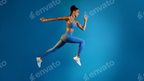 Preview: Determined Young Sportswoman Jumping Posing In Mid-Air On Blue Background