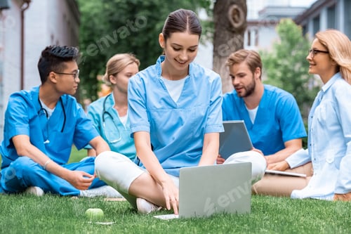 Preview: cheerful teacher and multicultural students studying outdoors with gadgets at medical university