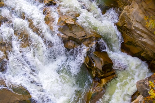 Preview: Aerial view of river waterfall with clear turquoise water falling down between wet boulders