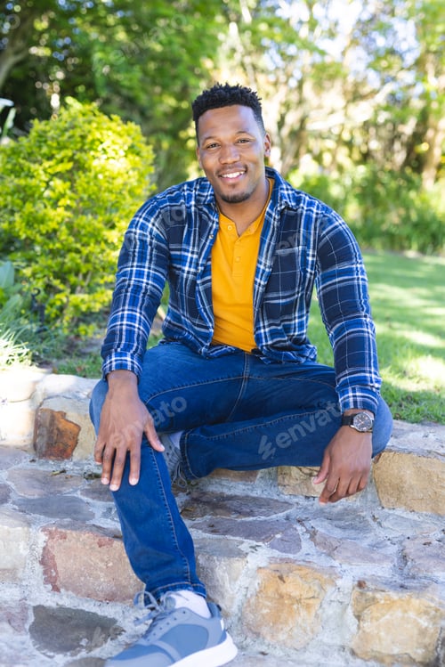 Preview: Happy african american man sitting on stairs in sunny garden, copy space