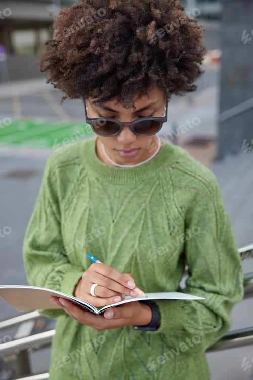 Preview: Clever curly female student writes ideas for university course uses notepad for education makes note