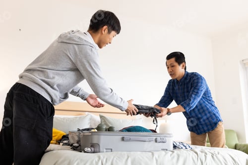 Preview: Father and son packing suitcase together on bed, preparing for travel adventure