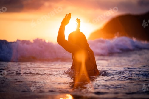 Preview: Silhouette of a woman wading in sea wave at sunset
