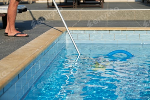 Preview: Male cleaning outdoor swimming pool with underwater vacuum tube