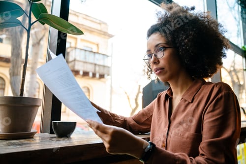 Preview: Young black woman with afro hairstyle holding paper documents in cafe