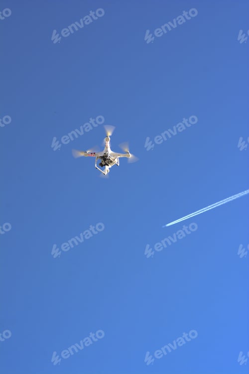 Preview: Vertical shot of a drone and plane trails in the blue sky