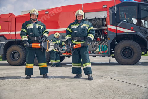 Preview: Strong handsome firefighters standing near the fire machine with equipment in hands