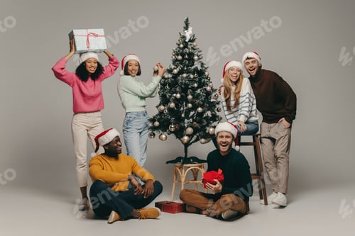 Visualização: Grupo de jovens sorrindo enquanto se divertem perto da árvore de Natal no fundo do estúdio juntos