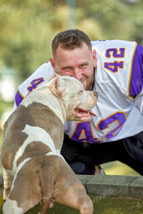 Preview: American football player with a dog posing on camera in a park. Copy space, sports banner. Concept