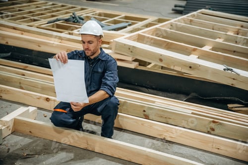Preview: Reading the plan. Male builder is at construction of wooden house