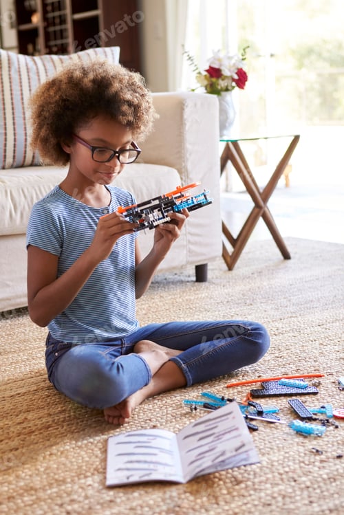 Preview: girl sitting on the floor in the living room building a toy from a construction kit, close up