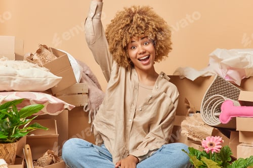 Preview: Real estate and ownership concept. Positive curly haired woman wears beige shirt keeps arm raised up