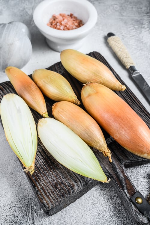 Preview: Raw cut baby shallot onion on a wooden board. White background. Top view