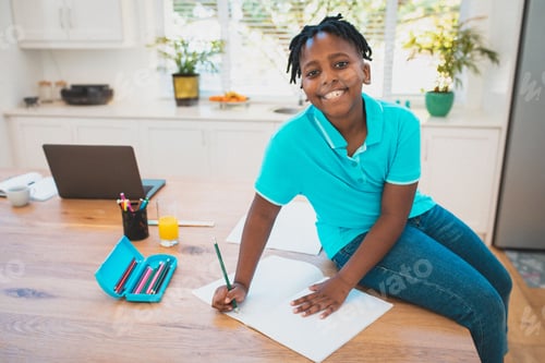 Preview: African American boy sitting on kitchen island at home writing in notebook with laptop, copy space