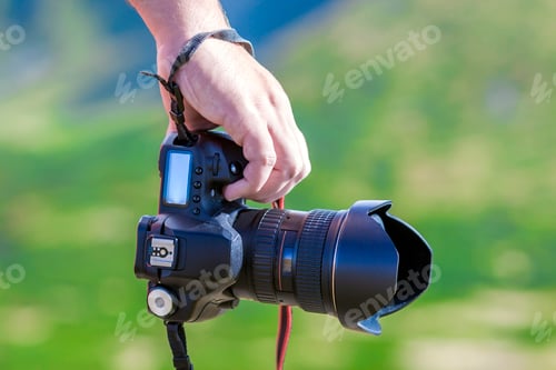 Preview: Hand of a man holding professional digital camera on blurred gre
