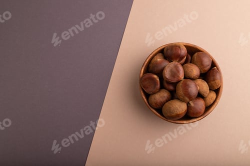 Preview: wooden bowl with raw edible Сhestnuts on brown and gray paper pastel, top view, flat lay, copy space
