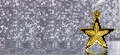 Preview: Gold bronze Christmas star on a defocused silver Christmas lights background with reflection.