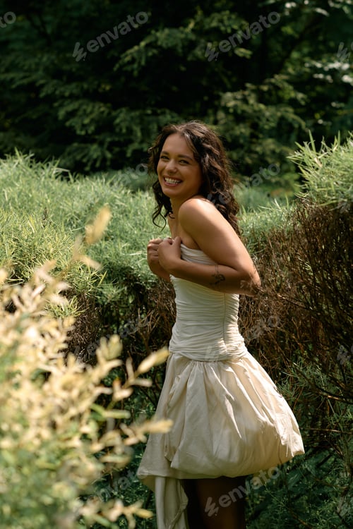 Vista previa: Young woman plays in a lush green garden wearing a beautiful white dress on a sunny day