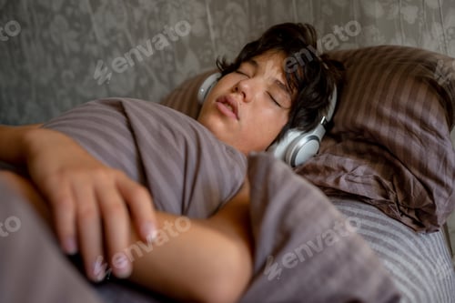 Preview: teenage boy sleeps at home on the couch listening to music with headphones