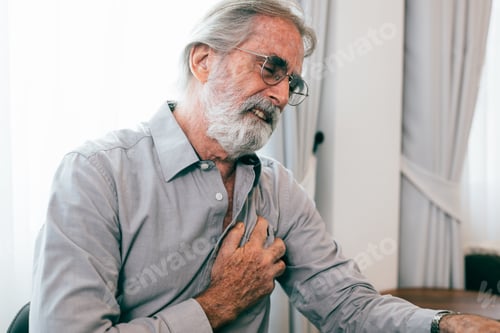 Preview: Senior man holding hand on chest and suffering from heart problem at home