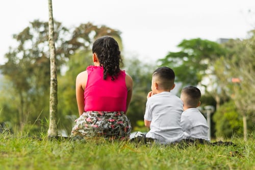 Preview: view of the back of two boys and a girl sitting on the lawn looking towards the horizon