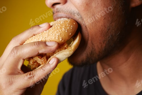 Preview: Man eating hamburger over yellow background