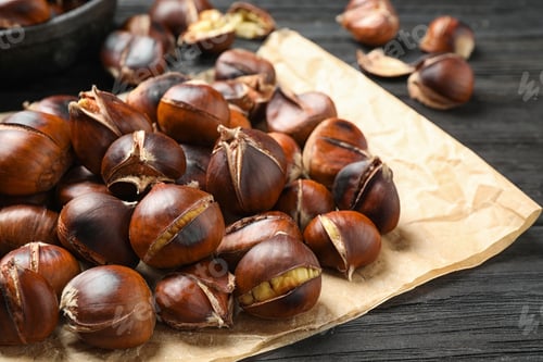 Preview: Tasty roasted edible chestnuts on black wooden table, closeup